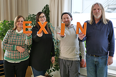 Teammitglieder halten orange Buchstaben hoch die das Wort EXIN bilden,
