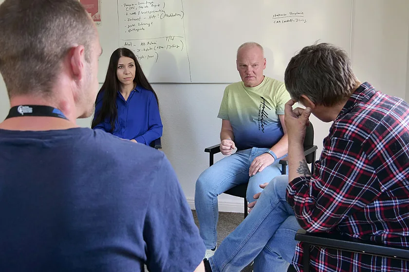 Die beiden Coaches sitzen vor einem Whiteboard. Im Vordergrund sieht man zwei Teilnehmende von hinten.