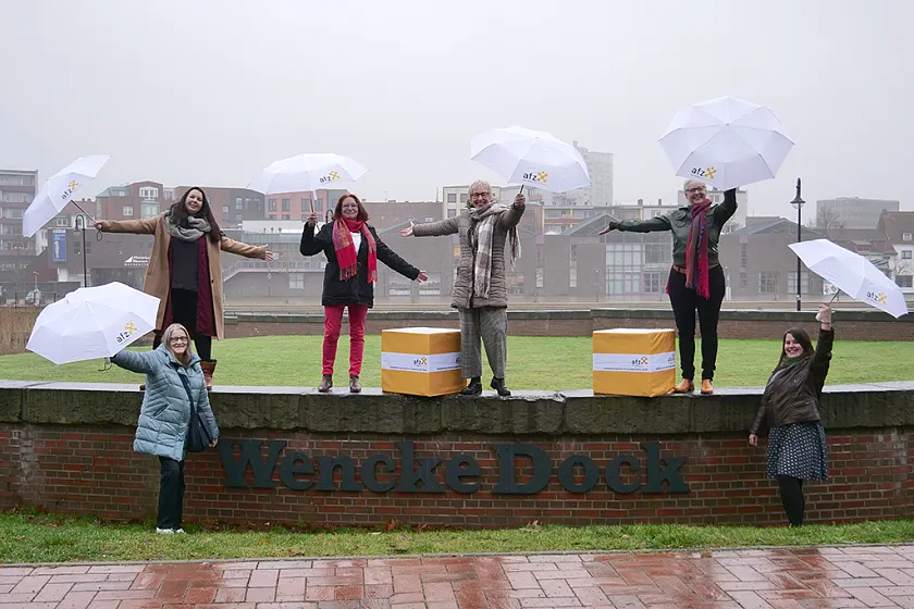 Team vom AFZ: die Frauen stehen mit Regenschirmen auf einer Mauer