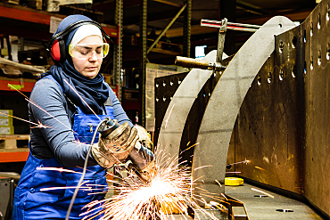 junge weibliche Auszubildende arbeitet mit einer Mühle in einer Werkstatt Funkenflug