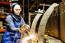 junge weibliche Auszubildende arbeitet mit einer Mühle in einer Werkstatt Funkenflug