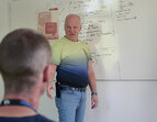 Coach erklärt etwas. Im Vordergrund Teilnehmenden von der Rückansicht. 
˜ Bildnachweis: eventfive GmbH, Indra Zilm